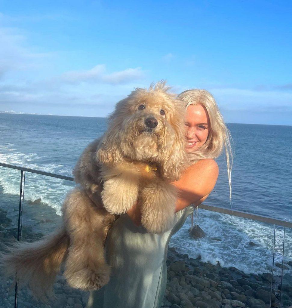Alex Cooper holding a dog in front of the ocean