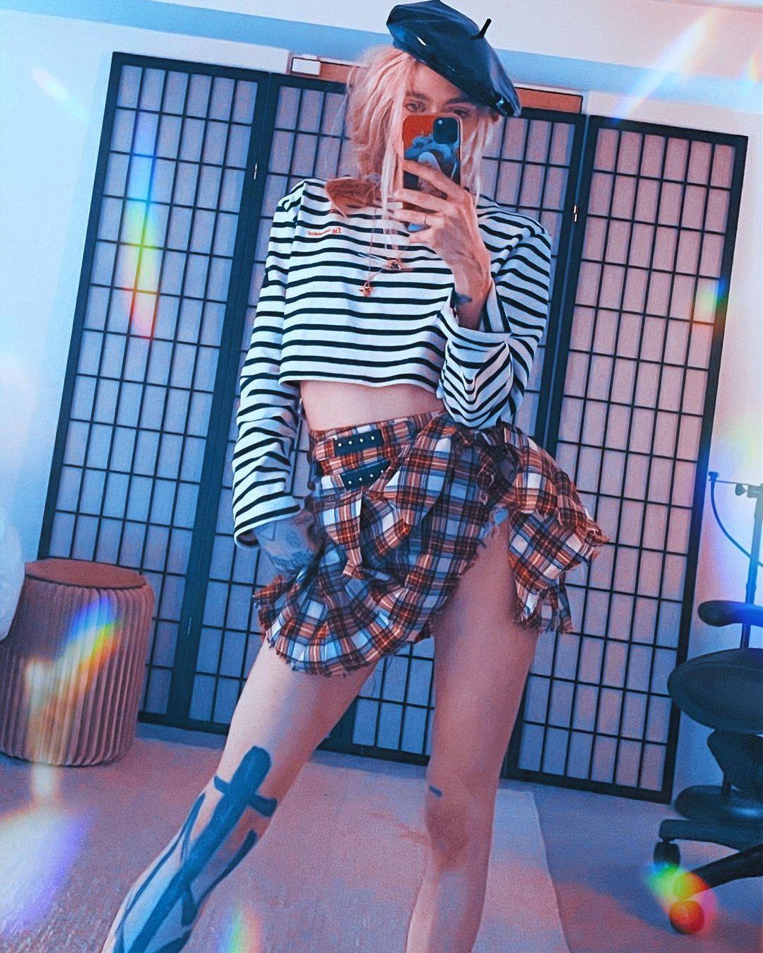 Grimes wearing a plaid skirt and striped shirt.