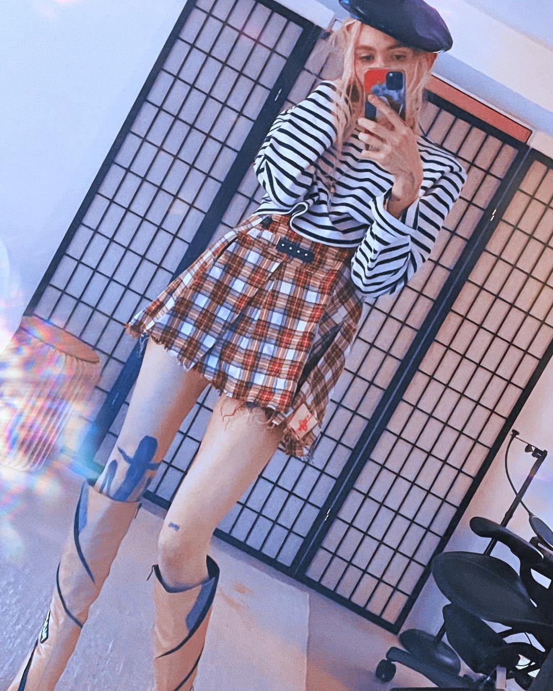 Grimes wearing a plaid skirt and striped shirt.