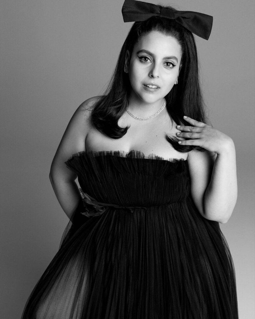A black and white themed photo showing Beanie Feldstein in a strapless black dress.