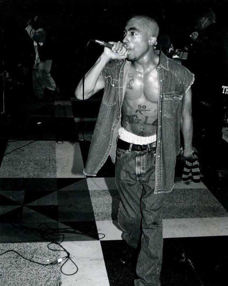 A black and white themed photo of Tupac Shakur performing on stage