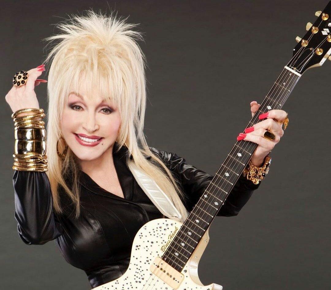 A photo of Dolly Parton in a black color outfit, holding a guitar.