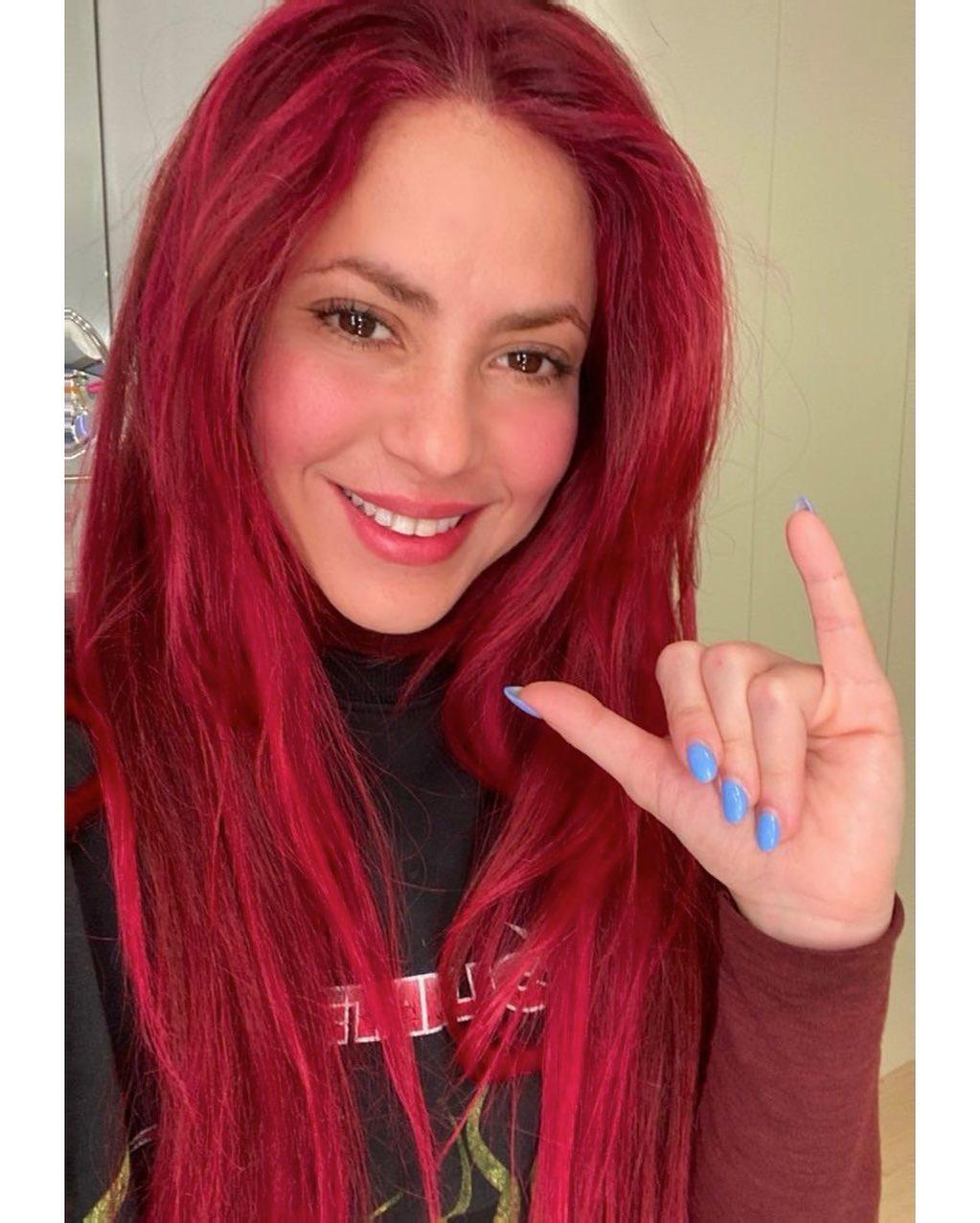 Shakira has long red hair and bright blue nails in a selfie.