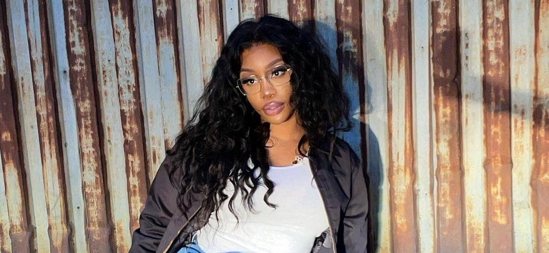 A photo showing SZA rocking a black jacket over a white shirt and denim pant.