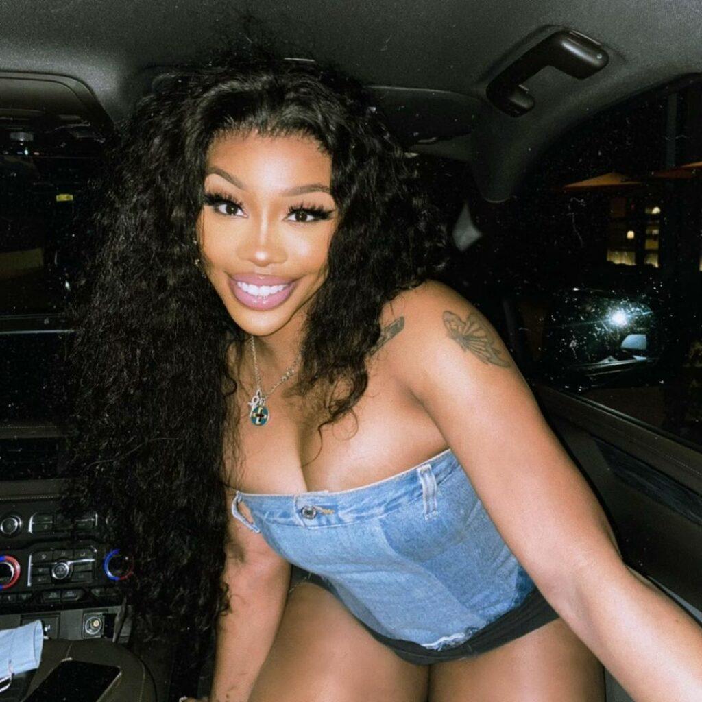 A photo showing SZA sporting a strapless denim blouse and black short in a vehicle