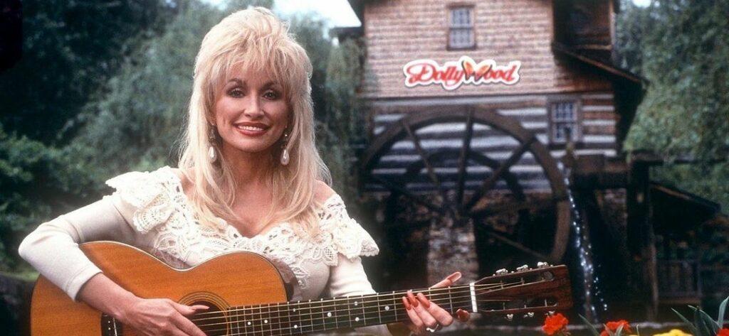 A photo showing Dolly Parton playing her guitar outside a house.