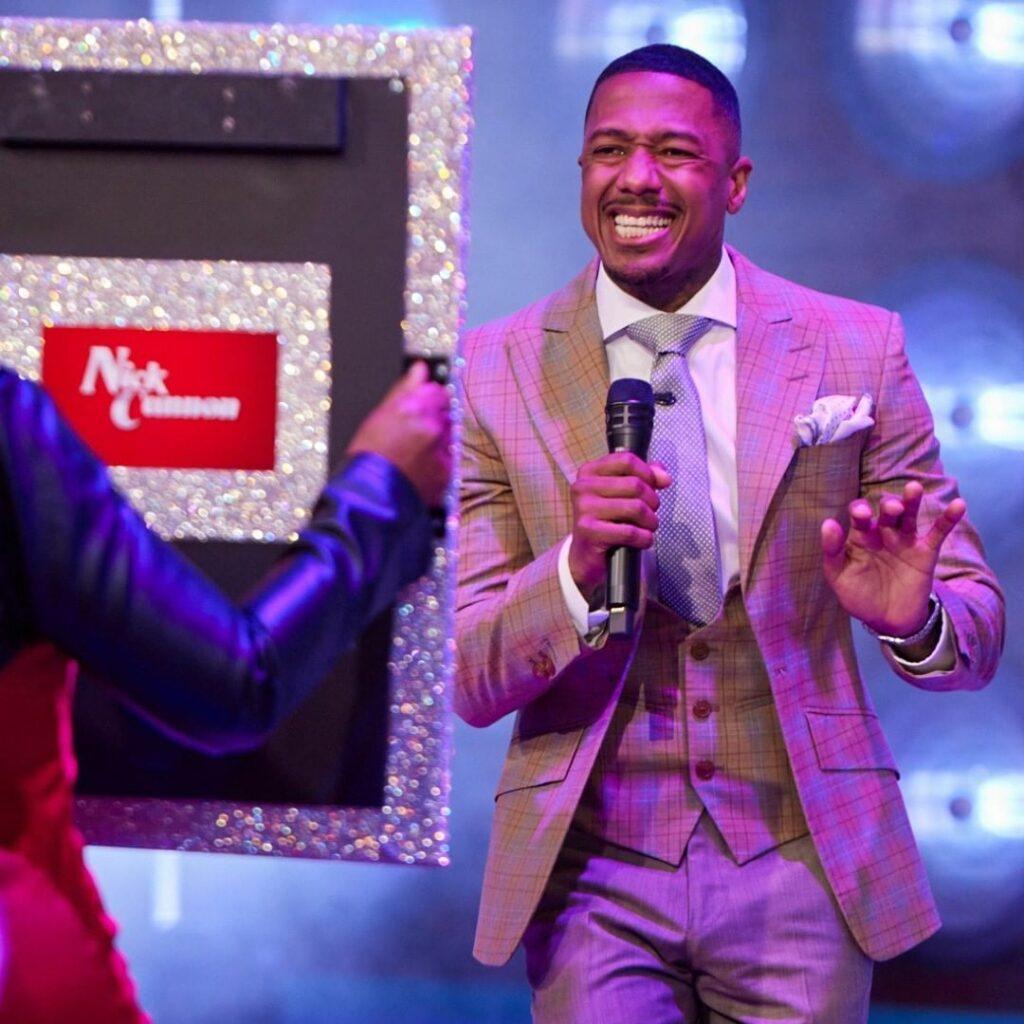 A photo of Nick Cannon holding a microphone, with a huge smile on his face.