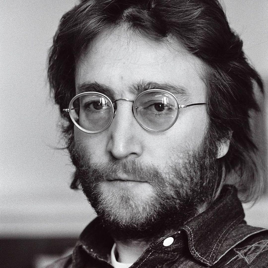 An amazing photo showing John Lennon sporting a pair of round-lens glasses in this black and white themed photo.