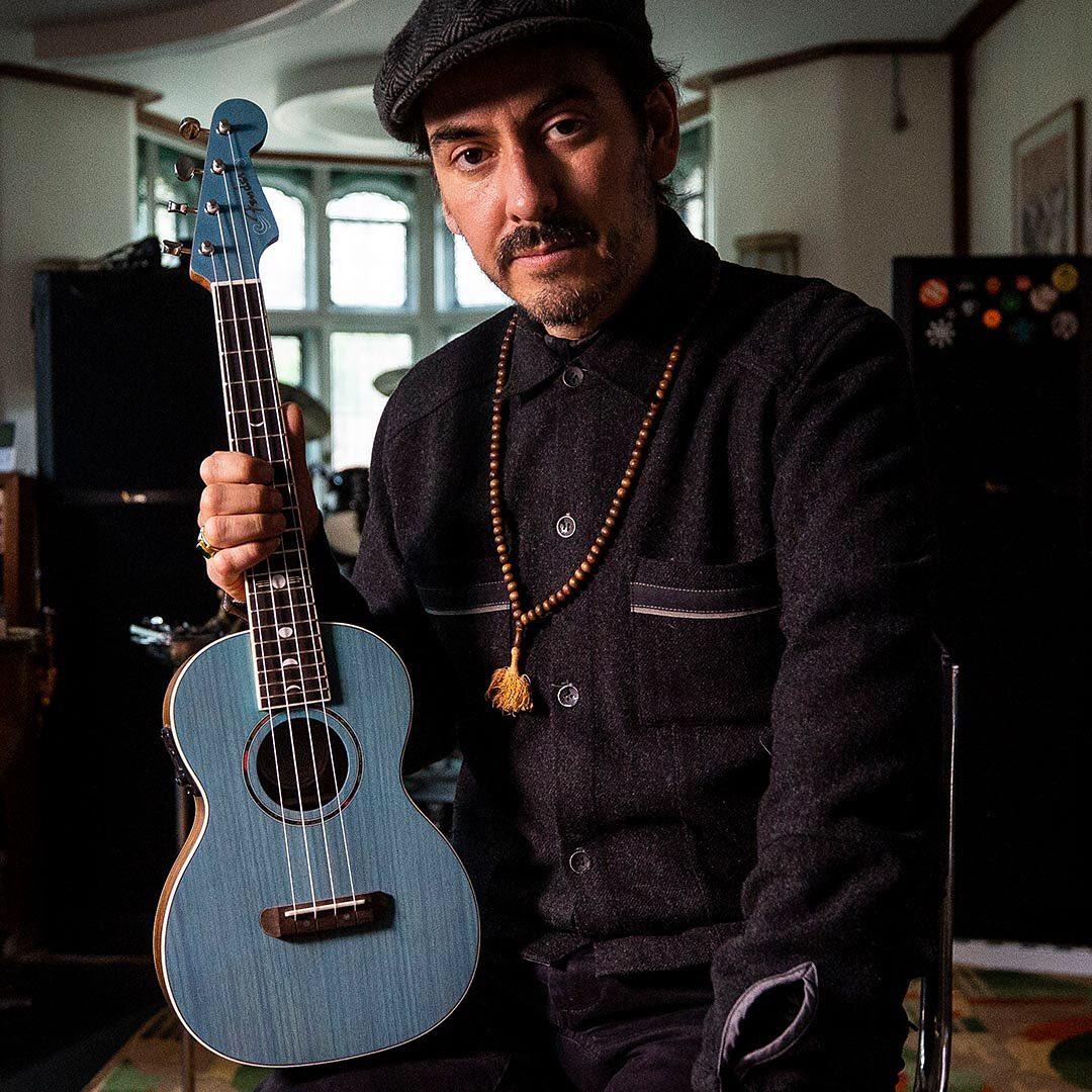 A photo showing Dhani Harrison holding a blue color guitar.