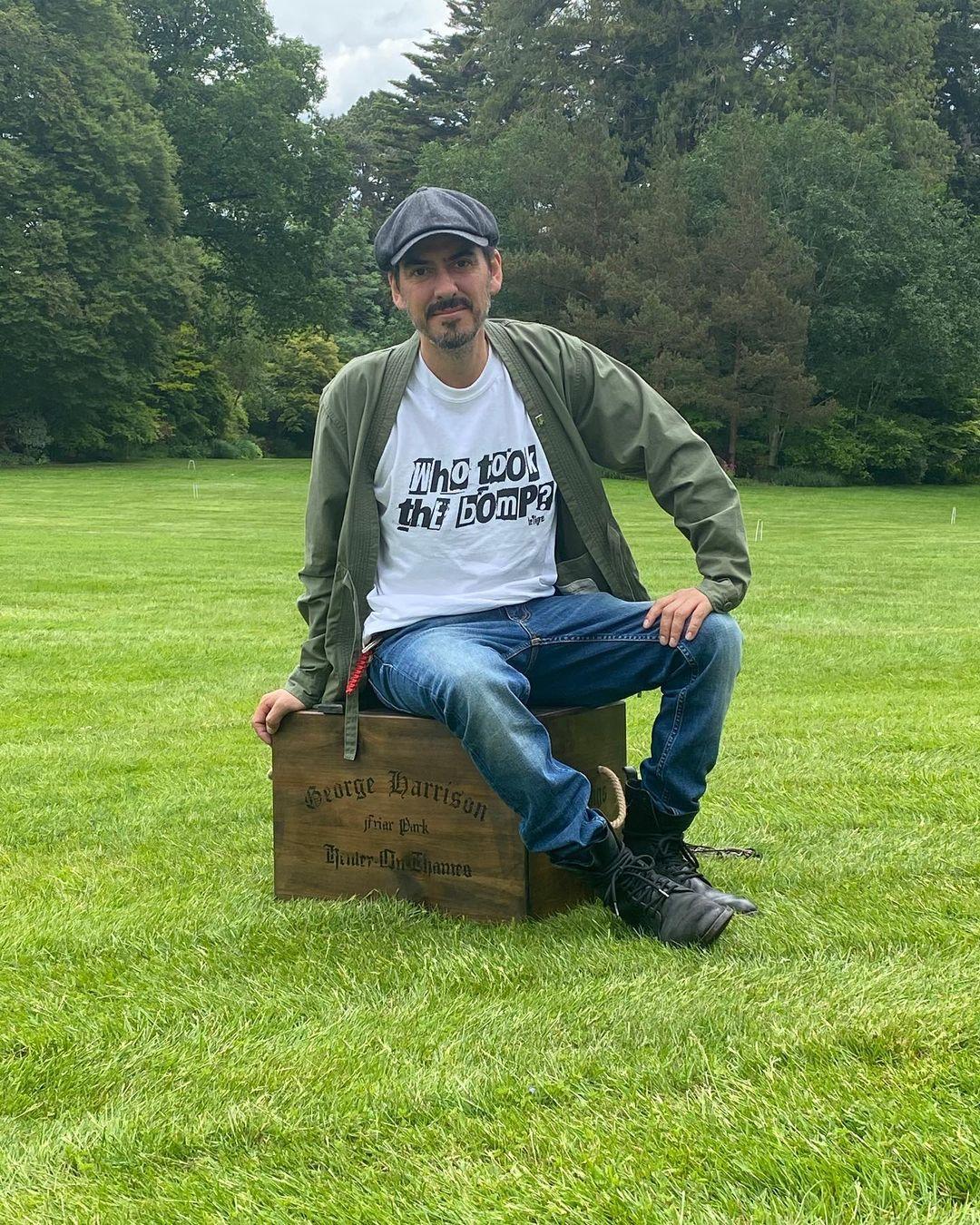 A photo showing Dhani Harrison sitting in a large field.