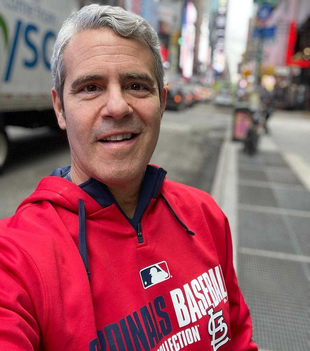 A selfie photo of Andy Cohen sporting a red hoodie on the street.