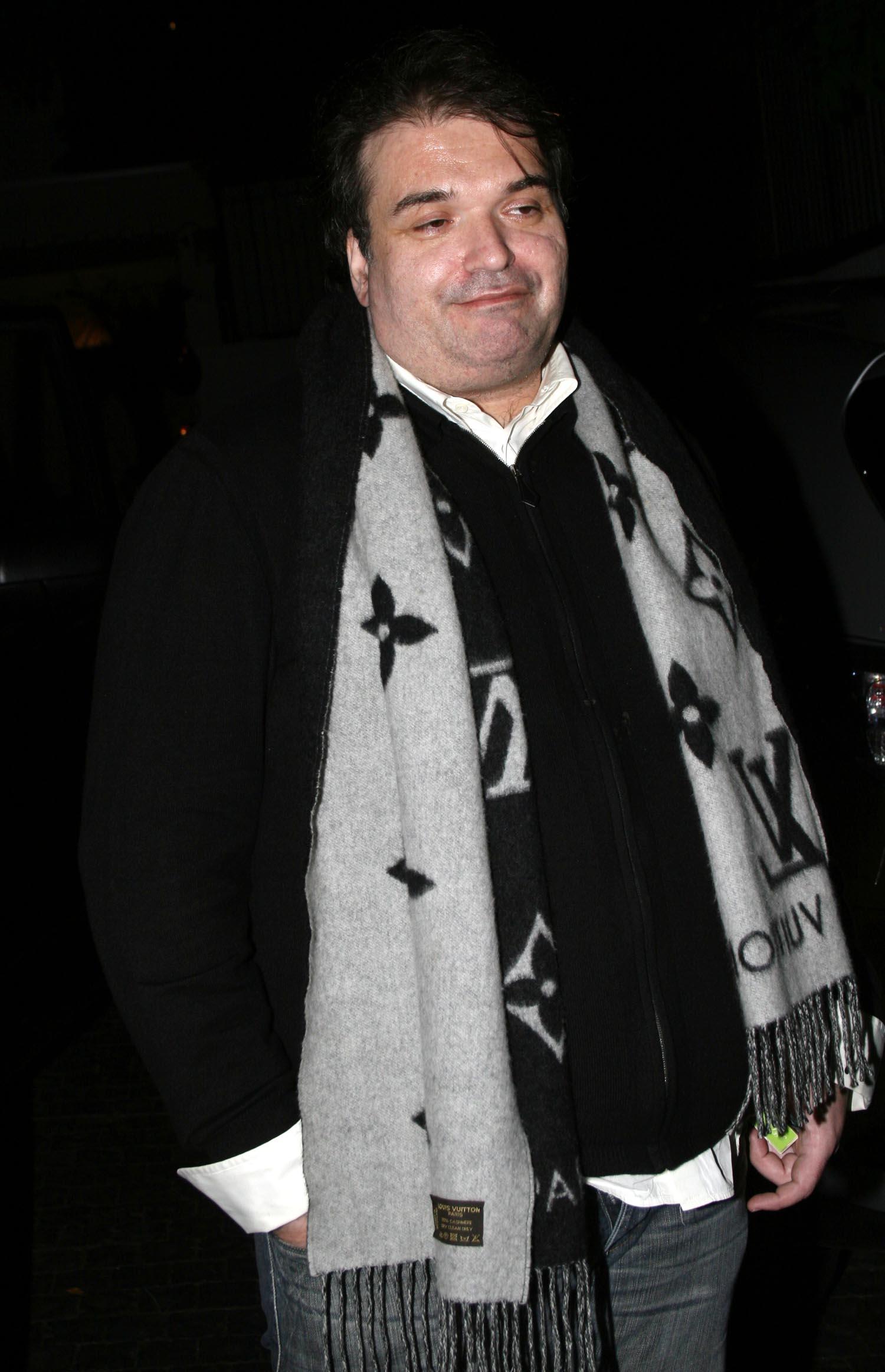 A photo showing Simon Monjack in a black sweater and gray color pant, with a matching scarf around his neck.