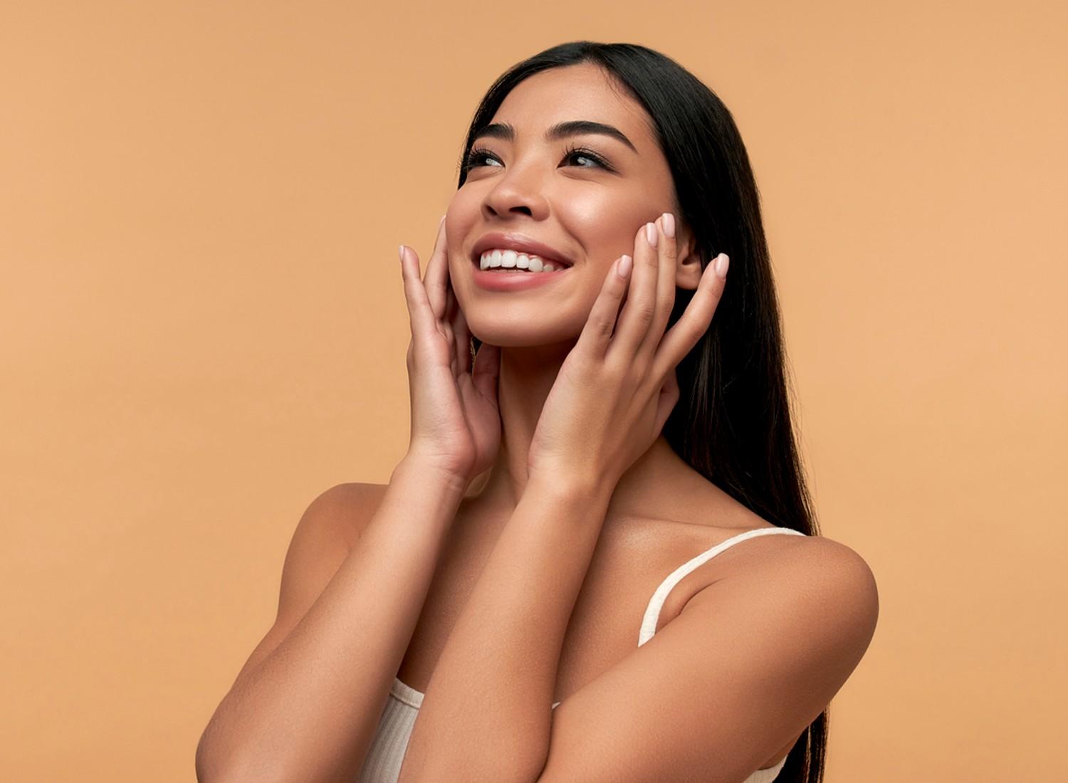 A tan woman smiling on a beige background.