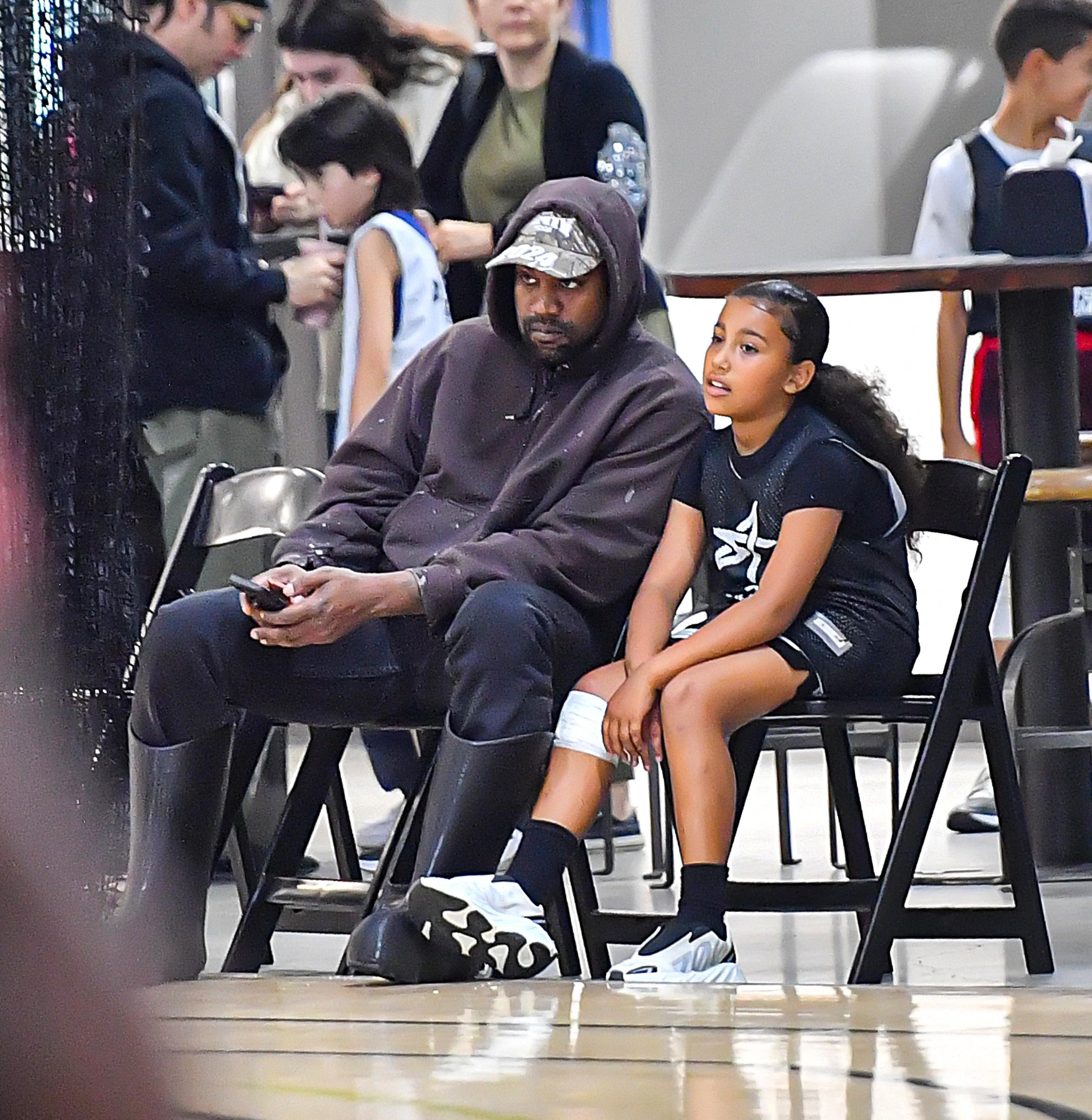 Kanye West com a filha North West em um jogo de basquete