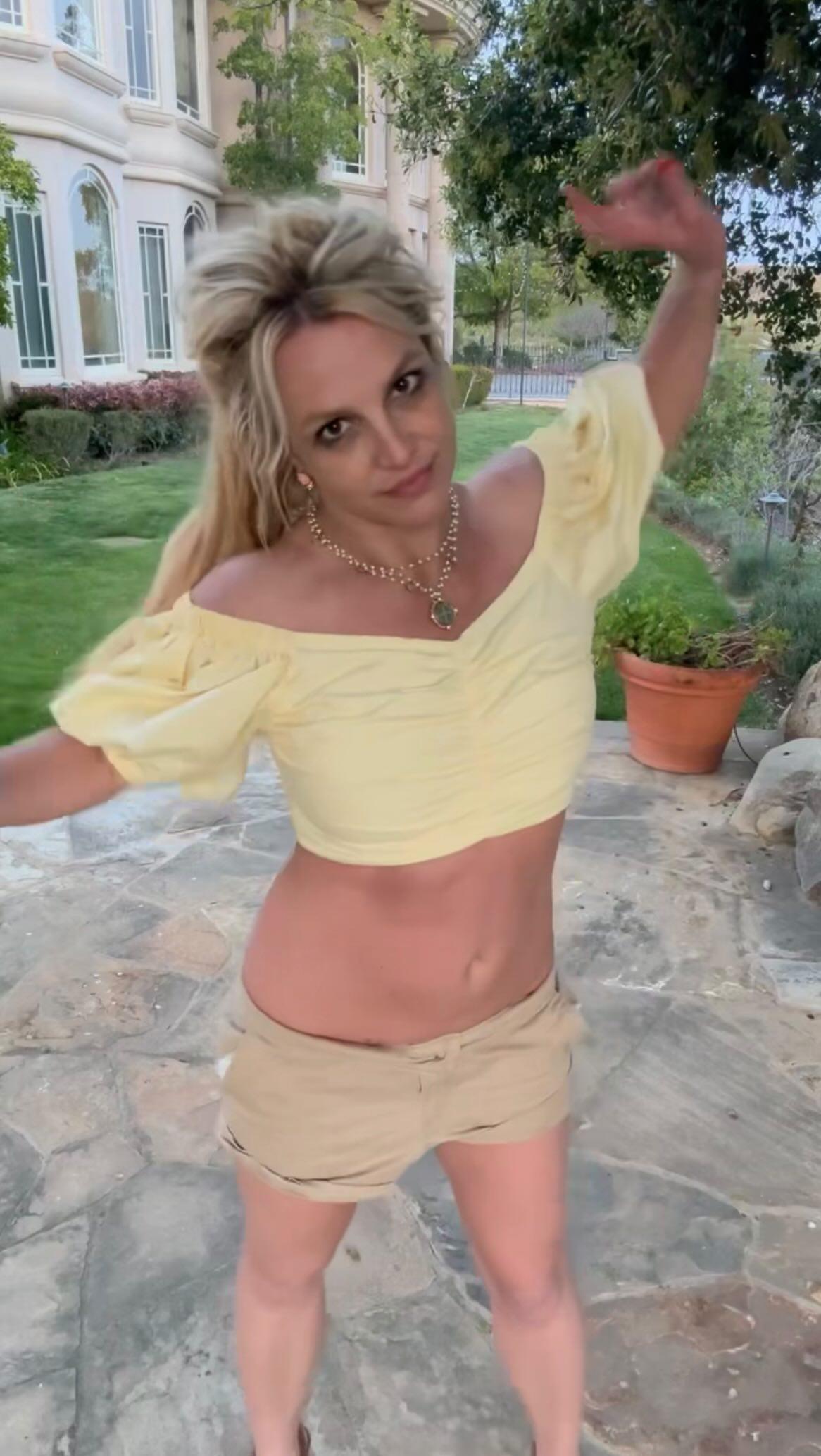 Britney Spears in a yellow top and brown shorts