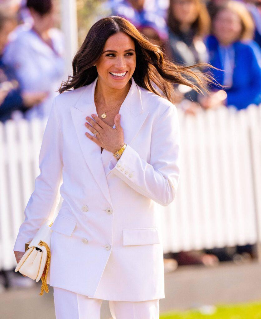 Meghan Markle smiling with her left hand on her chest
