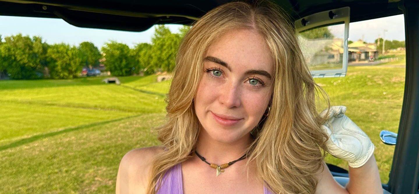 Grace Charis sits in a golf cart in a plunging purple crop top