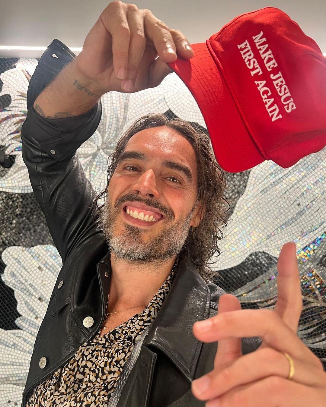 Russell Brand holds MAGA-like hat