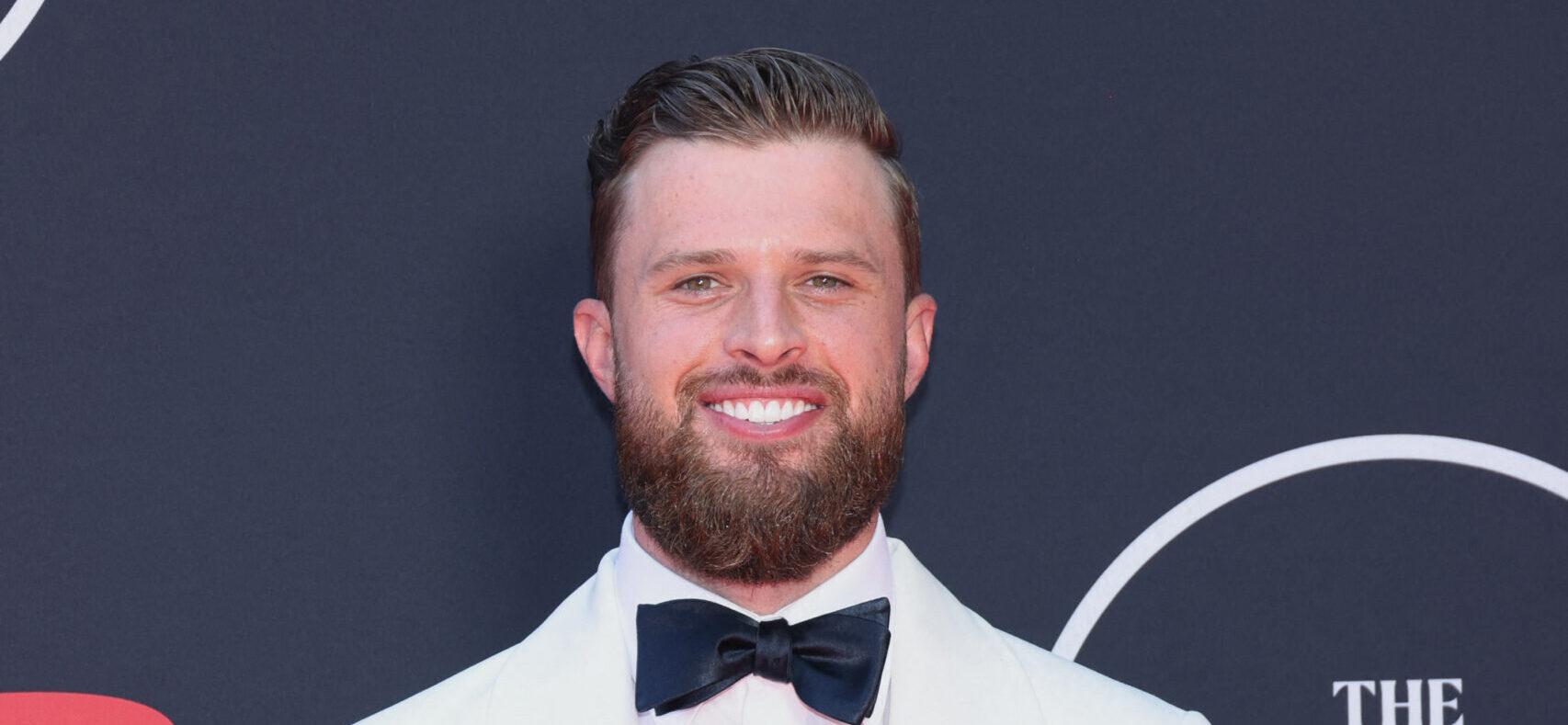 Harrison Butker smiling in a white suit on the red carpet.