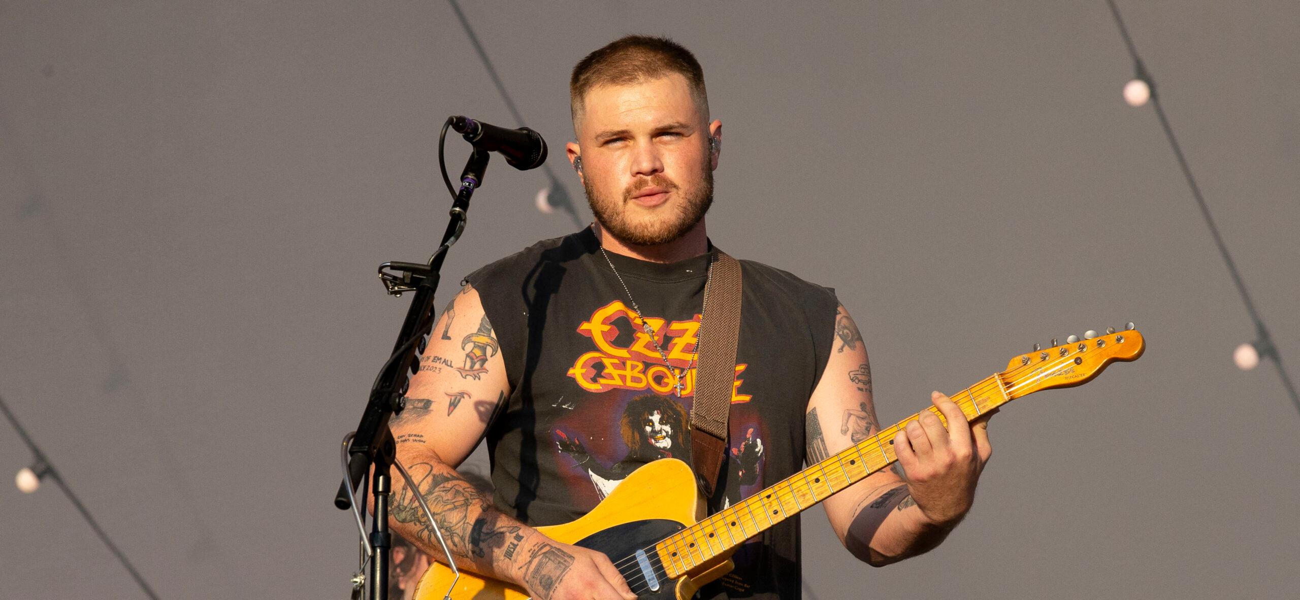 Zach Bryan playing guitar during a show.