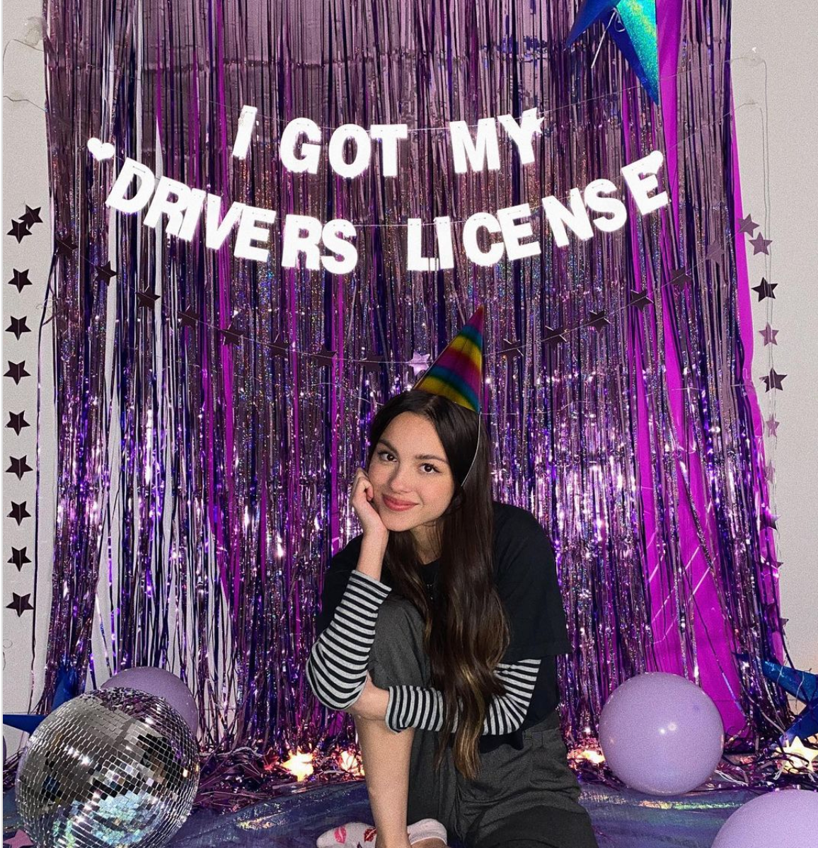 Olivia Rodrigo in front of a shiny driver's license sign