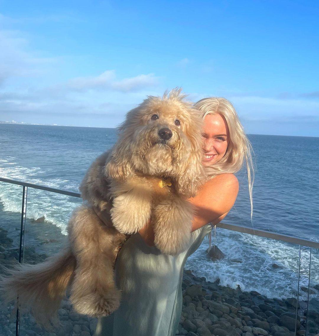 Alex Cooper holding a dog in front of the ocean