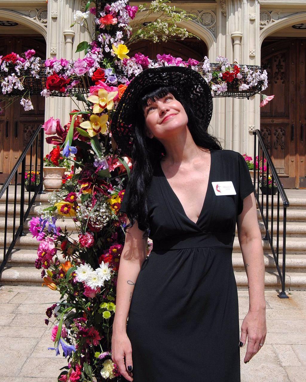 A photo of Pauley Perrette in a black dress, and behind her are multicolored flowers.