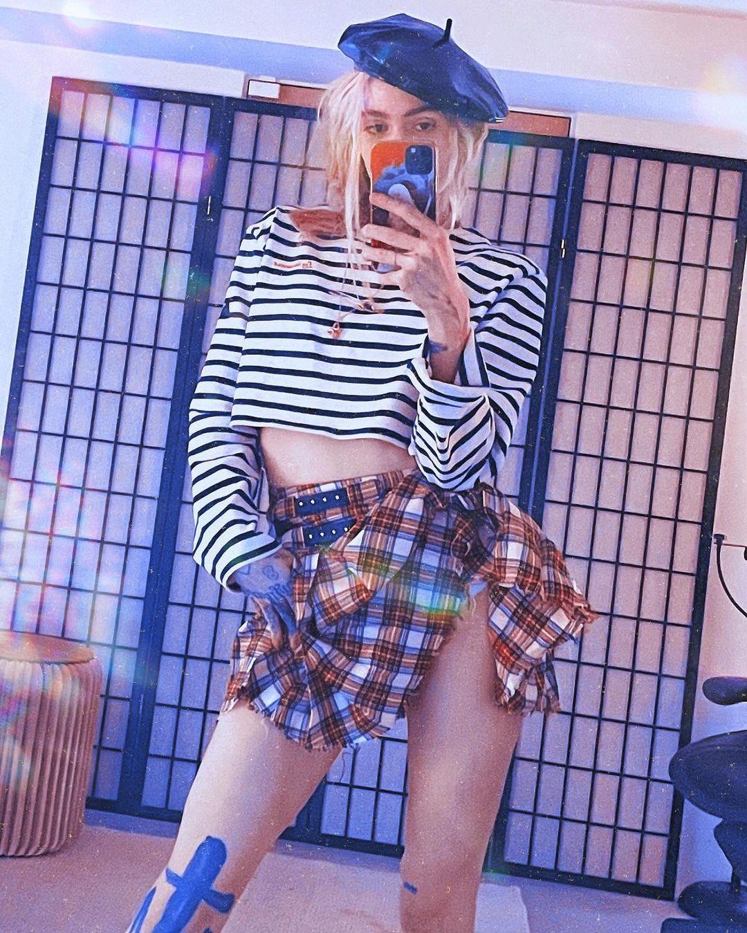 Grimes wearing a plaid skirt and striped shirt.