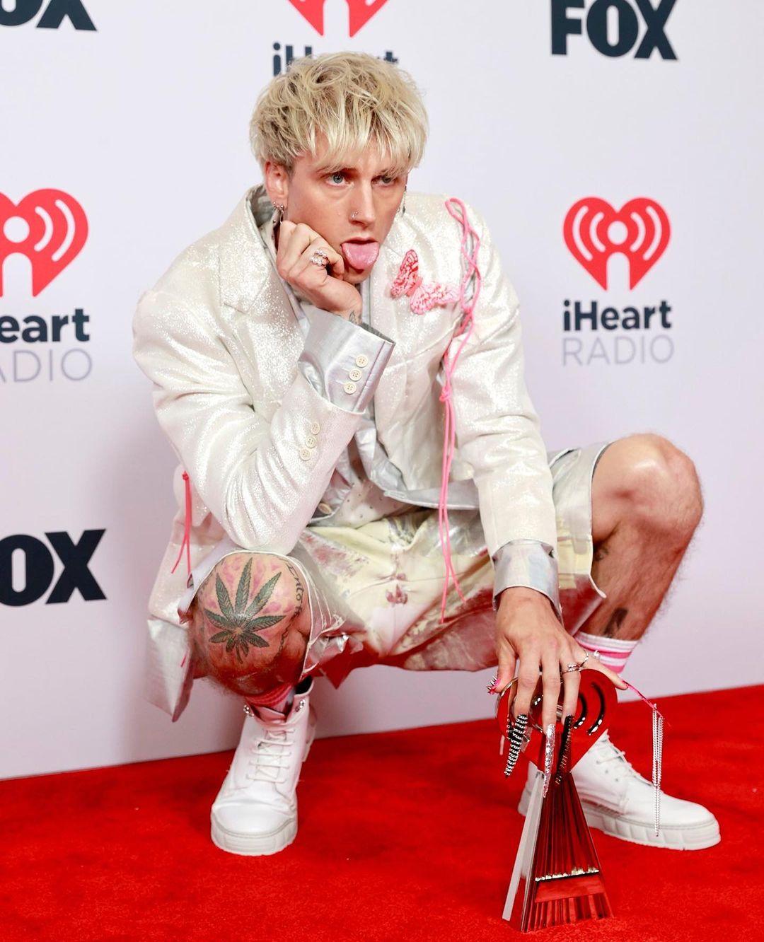 A photo showing Machine Gun Kelly in a crouched pose at a red carpet event.