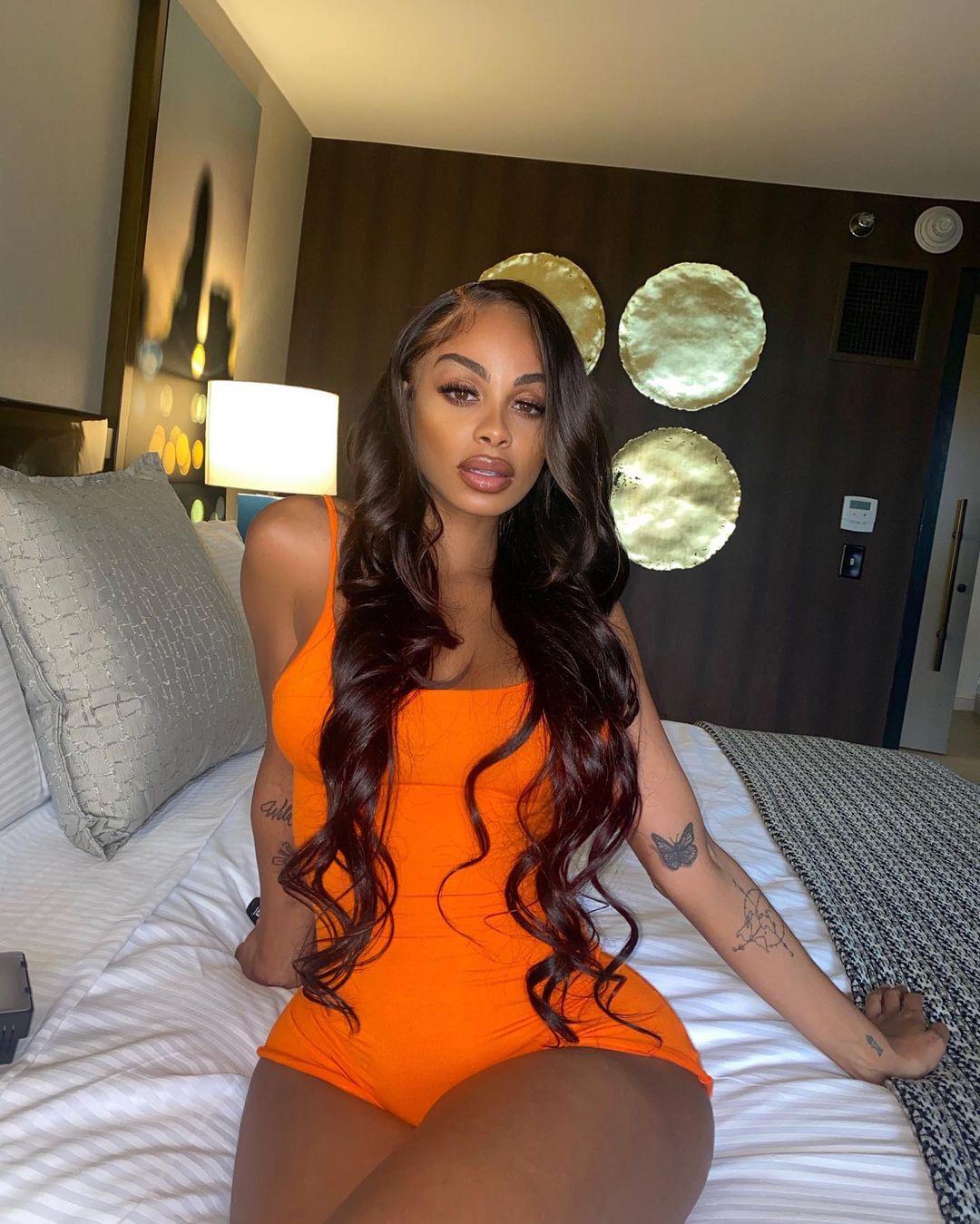 A photo showing Ana Montana sitting on a bed in an orange color outfit