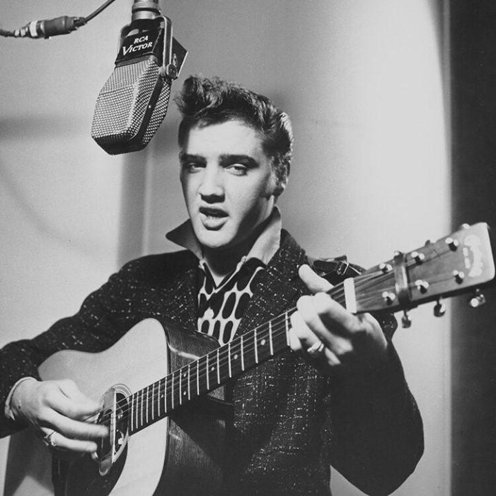 A photo of Elvis Presley singing into a microphone, while playing a guitar.
