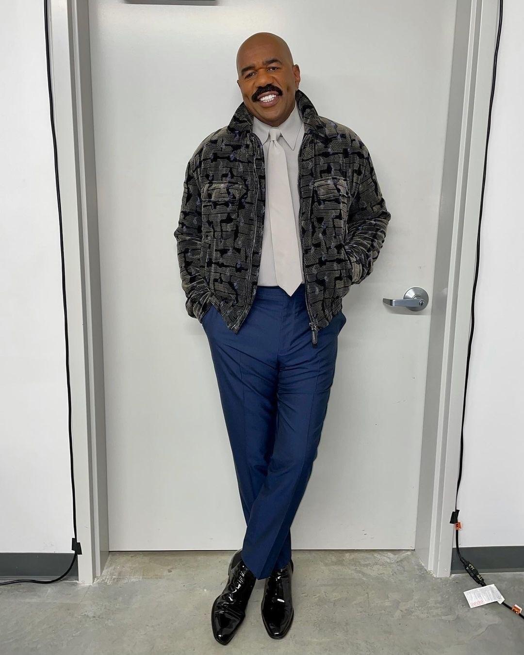 An amazing photo showing Steve Harvey in a gray jacket over a white shirt and blue pant.