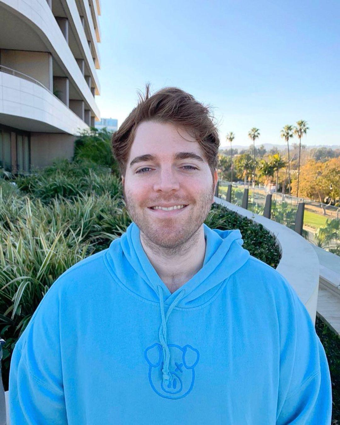A photo showing Shane Dawson rocking a light blue color hoodie with a smile on his face.