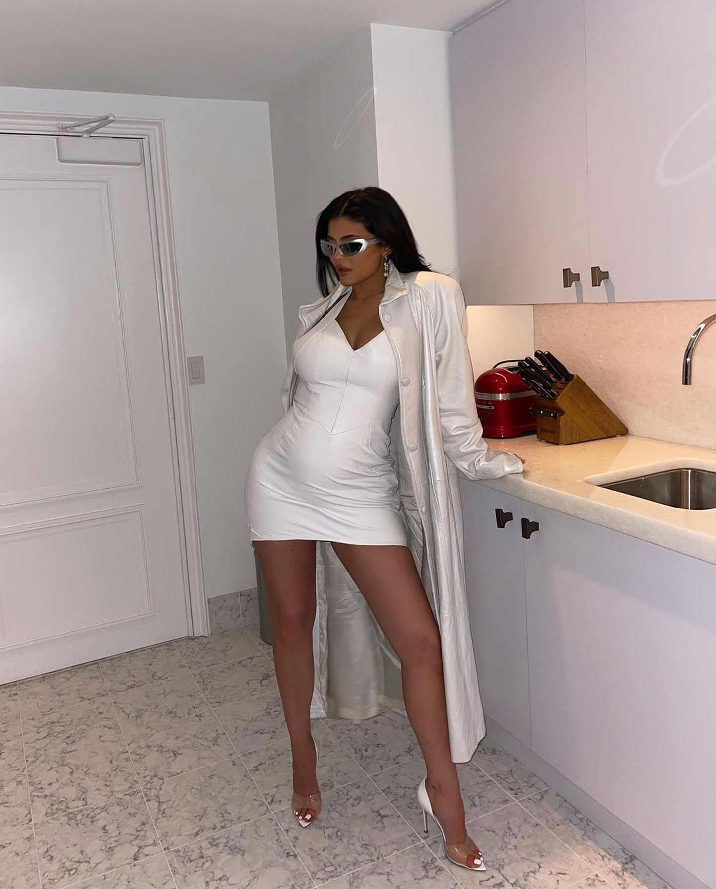 Kylie Jenner in a white latex outfit with her baby bump showing.