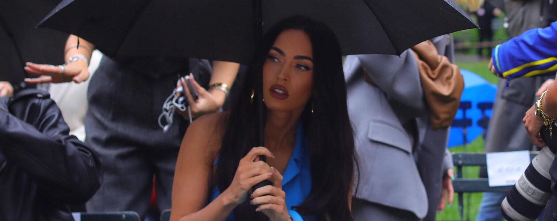 Megan Fox stuns in blue as she stares into the cameras while holding an umbrella in the rain during the Moschino fashion show held outside during fashion week in NYC