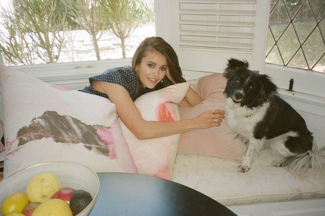 Nina Dobrev lies on the couch with her dog while hugging a pillow to her chest.