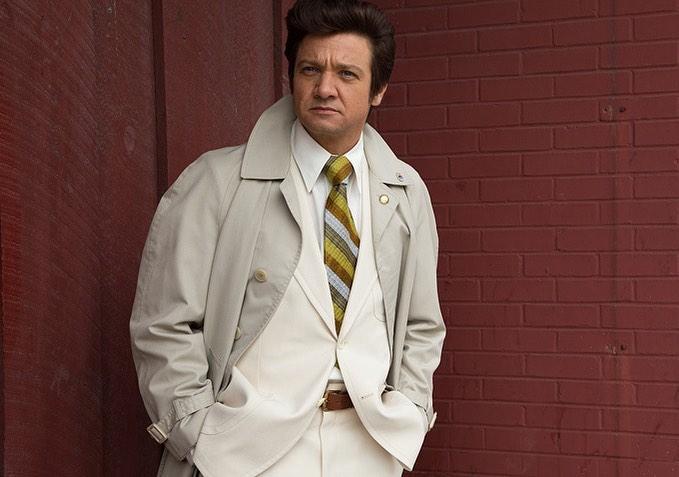 A photo of Jeremy Renner in a creme color outfit, with a striped tie.