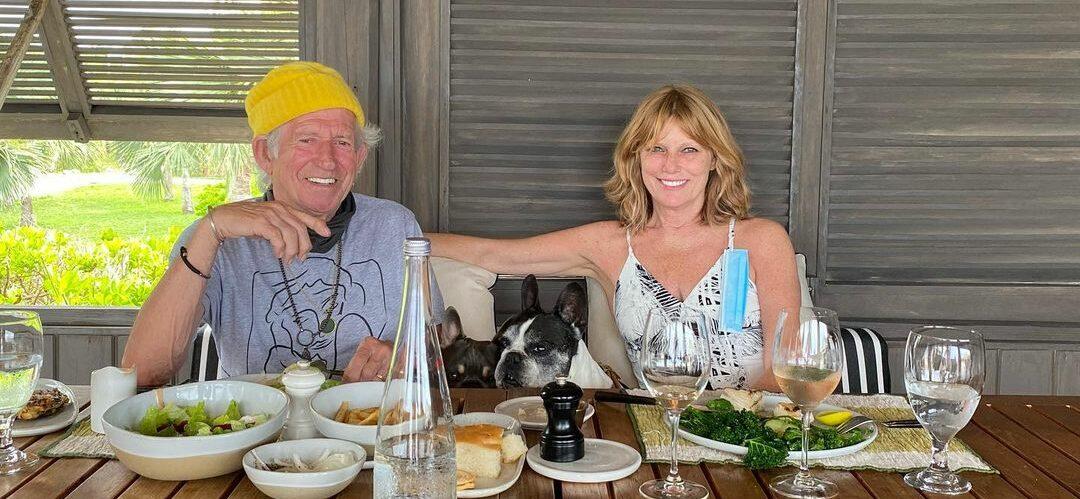 A photo showing Keith Richards and Patti Hansen eating on a large wooden table.