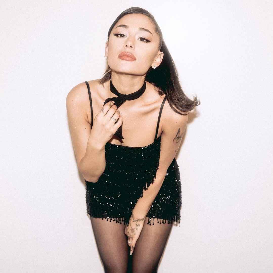 Ariana Grande leans over to pose for a photo wearing a skimpy black dress.