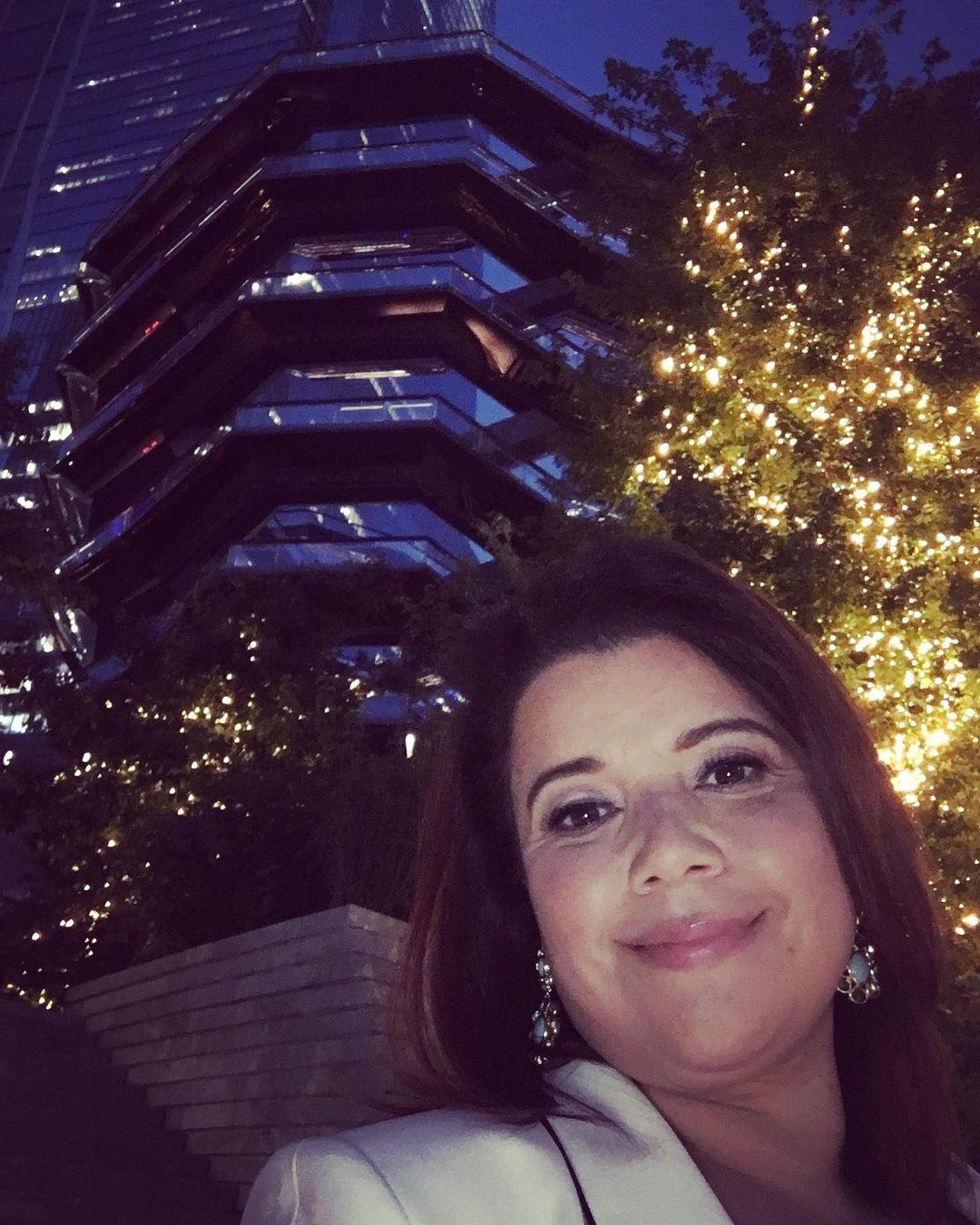 A lovely photo showing Ana Navarro out at night in front of a shiny sky-scraper behind her.