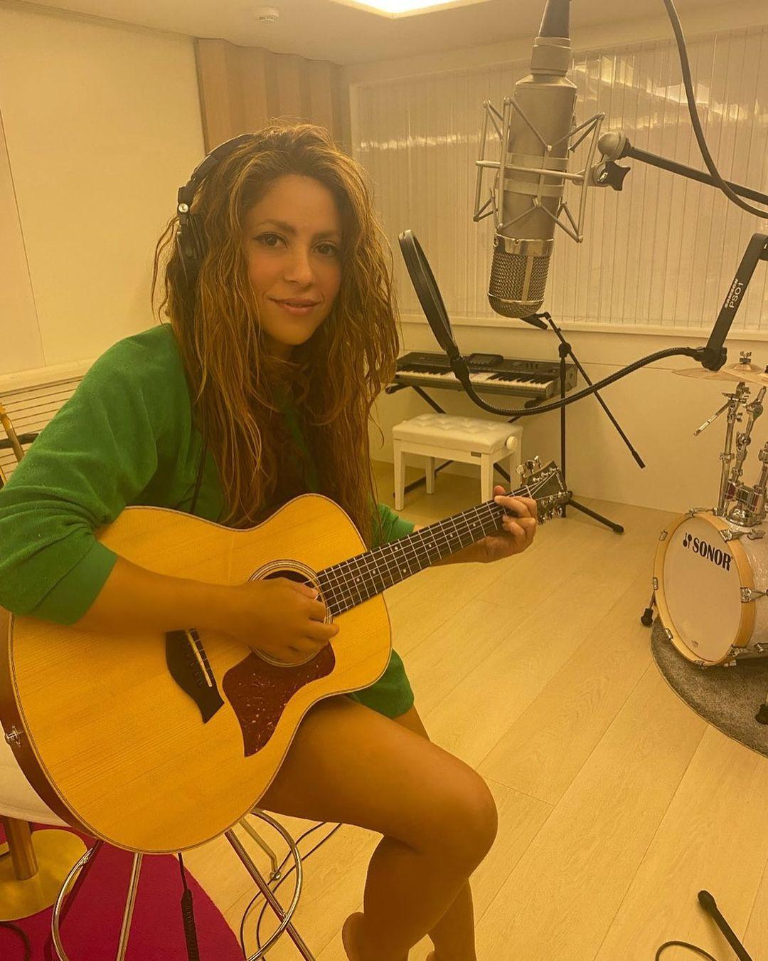 Shakira is playing acoustic guitar in a small recording studio.