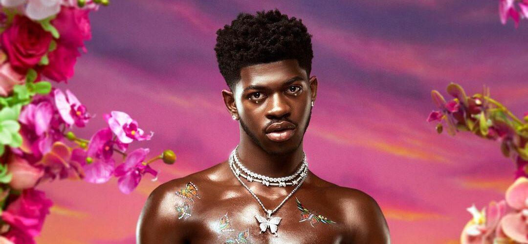 A photo showing bare-chested Lil Nas X in a garden filled with colorful flowers.