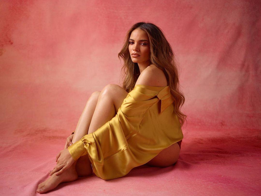 A photo of Leslie Grace sitting in a yellow dress.