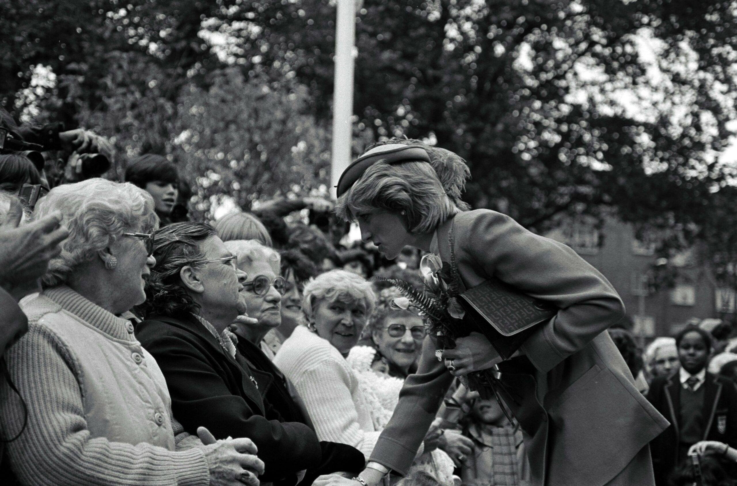 A black and white themed photo showing Princess Diana greeting people.