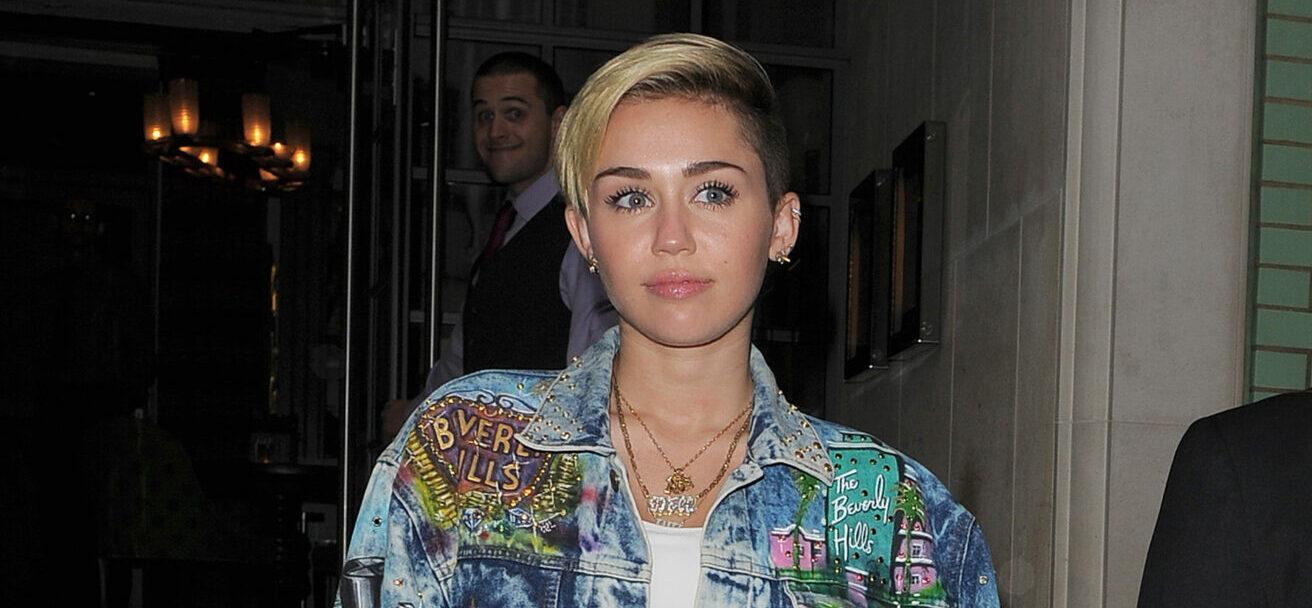 Miley Cyrus leaves her hotel arm in arm with her bodyguard The singer was wearing a white crop top black knee high boots denim hot pants and a matching denim jacket