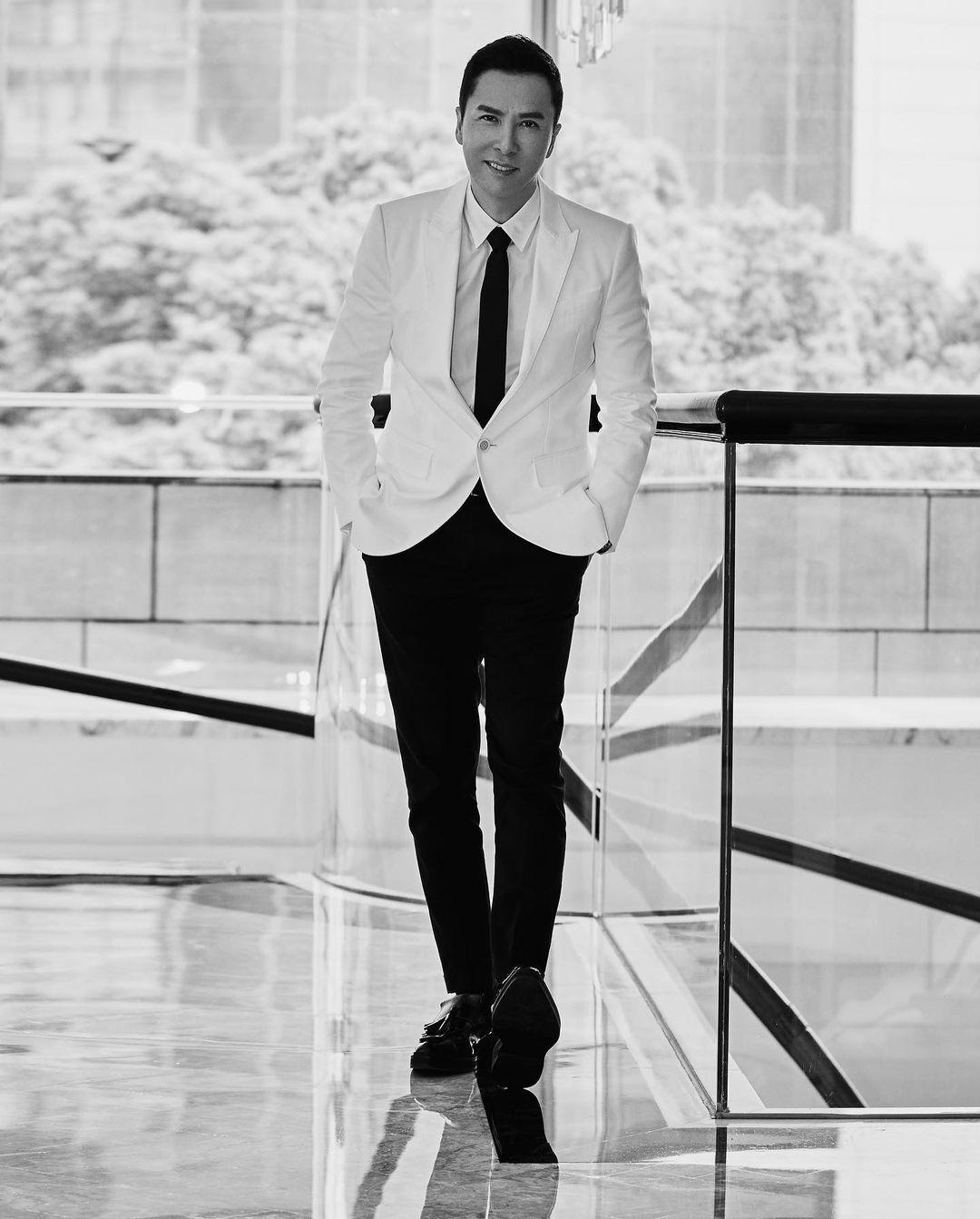 A black and white themed photo of Donnie Yen in a white suit and black pant.