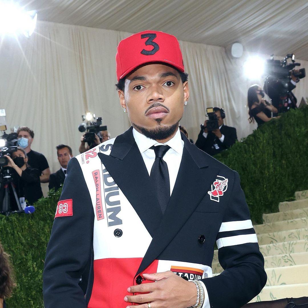 A photo showing Chance The Rapper at an awards event in a black and red design suit.