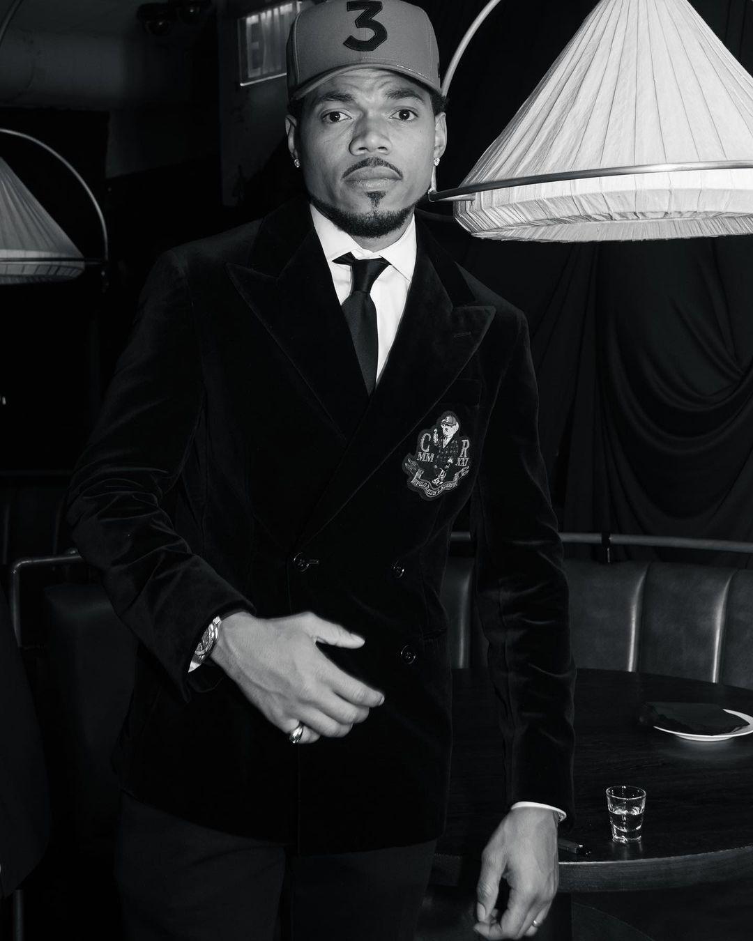 A black and white themed photo showing Chance The Rapper in a suit and hat.