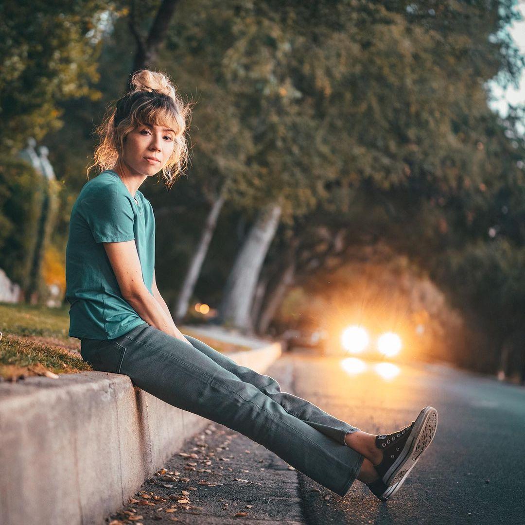 A photo showing Jennette McCurdy sitting on a pedestrian pavement by the roadside.