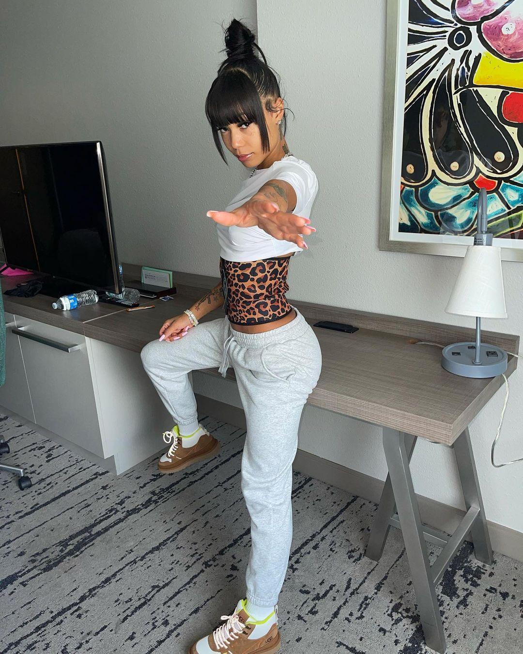 A photo showing Coi Leray in a gray sweat-pant and white crop-top.
